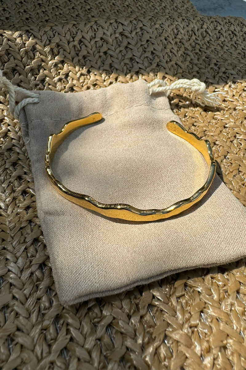Wellenf&ouml;rmiger goldener Armreif aus Edelstahl mit hochwertiger 14-Karat-Vergoldung. Das elegante, offene Design passt sich m&uuml;helos jedem Handgelenk an und sorgt f&uuml;r hohen Tragekomfort. Der moderne Damen-Armreif kann einzeln getragen oder f&uuml;r einen individuellen Layering-Look mit weiteren Armreifen kombiniert werden. Zeitloser Schmuck in edler Goldoptik f&uuml;r Alltag und besondere Anl&auml;sse.