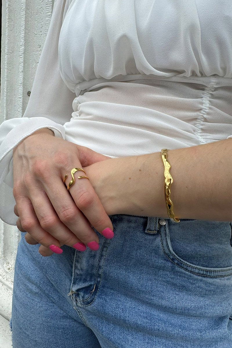 Wellenf&ouml;rmiger goldener Armreif aus Edelstahl mit hochwertiger 14-Karat-Vergoldung. Das elegante, offene Design passt sich m&uuml;helos jedem Handgelenk an und sorgt f&uuml;r hohen Tragekomfort. Der moderne Damen-Armreif kann einzeln getragen oder f&uuml;r einen individuellen Layering-Look mit weiteren Armreifen kombiniert werden. Zeitloser Schmuck in edler Goldoptik f&uuml;r Alltag und besondere Anl&auml;sse.