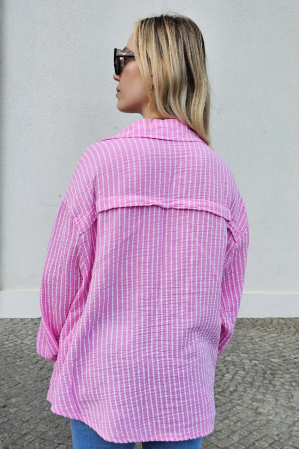 Gestreifte, lockere Bluse in rosa aus 100% Baumwolle, gefertigt aus weichem Musselinstoff. Die Bluse hat einen Oversize-Schnitt, der für einen lässigen Look sorgt. Sie besitzt einen V-Ausschnitt mit Umlegekragen und eine durchgehende Knopfleiste. Hinten ist eine querlaufende Falte eingearbeitet, die für zusätzliche Struktur sorgt. Die Bluse hat eine mittlere Länge und lange Ärmel mit 1-Knopf-Manschetten an den Ärmelenden.