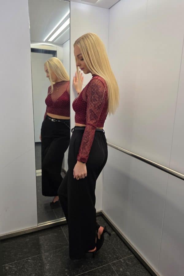 Zartes, bordeaux-farbenes Mesh-Oberteil mit langen transparenten Ärmeln und feinen glitzernden Punkten. Unter dem durchsichtigen Tüll befindet sich ein integriertes, leicht gepolstertes Bralette-Crop-Top im gleichen Farbton. Das Oberteil wirkt feminin, leicht und elegant.