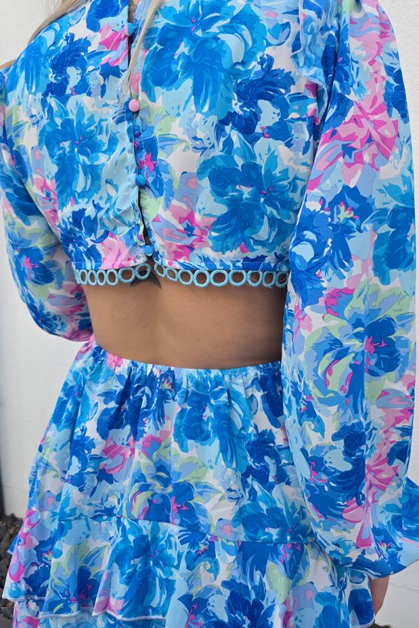 Sommerliches Minikleid mit floralem Muster in Blau- und Rosatönen, kurzem A-Linien-Rock und tiefem V-Ausschnitt für eine feminine Silhouette. Lange Puffärmel mit elastischen Bündchen sorgen für luftigen Tragekomfort. Seitliche Cut-outs und ein offener Rücken mit zarten gehäkelten Spitzeneinsätzen verleihen dem Kleid eine verspielte Boho-Note. Der stufige Volant-Rock und die kurze Passform machen das Kleid ideal für warme Tage und lässige Sommerlooks.