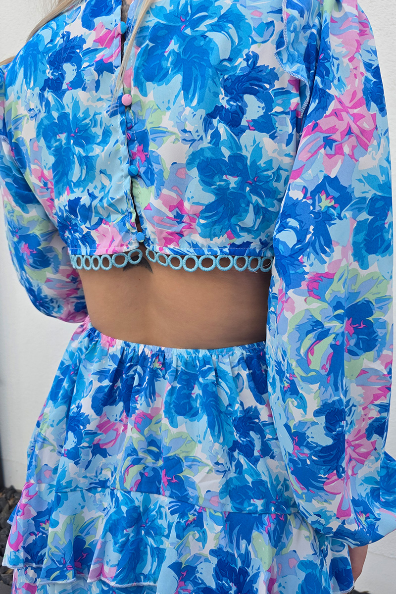 Sommerliches Minikleid mit floralem Muster in Blau- und Rosatönen, kurzem A-Linien-Rock und tiefem V-Ausschnitt für eine feminine Silhouette. Lange Puffärmel mit elastischen Bündchen sorgen für luftigen Tragekomfort. Seitliche Cut-outs und ein offener Rücken mit zarten gehäkelten Spitzeneinsätzen verleihen dem Kleid eine verspielte Boho-Note. Der stufige Volant-Rock und die kurze Passform machen das Kleid ideal für warme Tage und lässige Sommerlooks.
