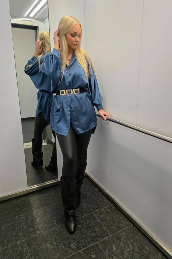 Dunkelblaue Oversize Damenbluse aus weich fließendem, leicht glänzendem Stoff. Die Bluse hat lange Fledermausärmel, eine klassische Knopfleiste vorne und einen dezenten Stehkragen. Der verlängerte, abgerundete Saum am Rücken sorgt für einen modernen, eleganten Look. Ideal für Büro, Alltag oder festliche Anlässe, mit lockerer Passform für maximalen Tragekomfort.