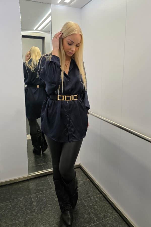 Dunkelblaue Oversize Damenbluse aus weich fließendem, leicht glänzendem Stoff. Die Bluse hat lange Fledermausärmel, eine klassische Knopfleiste vorne und einen dezenten Stehkragen. Der verlängerte, abgerundete Saum am Rücken sorgt für einen modernen, eleganten Look. Ideal für Büro, Alltag oder festliche Anlässe, mit lockerer Passform für maximalen Tragekomfort.