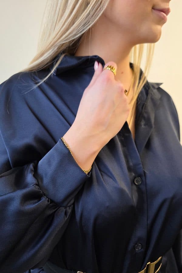 Dunkelblaue Oversize Damenbluse aus weich fließendem, leicht glänzendem Stoff. Die Bluse hat lange Fledermausärmel, eine klassische Knopfleiste vorne und einen dezenten Stehkragen. Der verlängerte, abgerundete Saum am Rücken sorgt für einen modernen, eleganten Look. Ideal für Büro, Alltag oder festliche Anlässe, mit lockerer Passform für maximalen Tragekomfort.