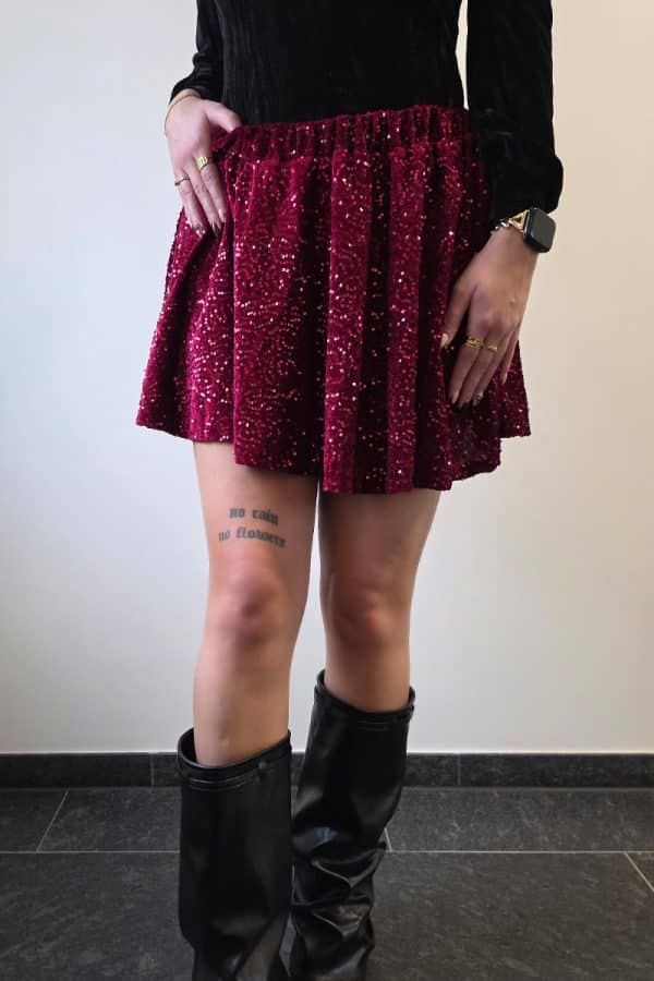 Weinroter Paillettenrock aus weichem Samt für Damen, mit intensiv funkelnder Glitzeroberfläche und elastischem Bund. Festlicher Minirock im A-Linien-Schnitt, ideal als Partyrock, Glitzerrock oder eleganter Rock für besondere Anlässe. Der Rock besitzt eingenähte Shorts für Sichtschutz und maximalen Tragekomfort.