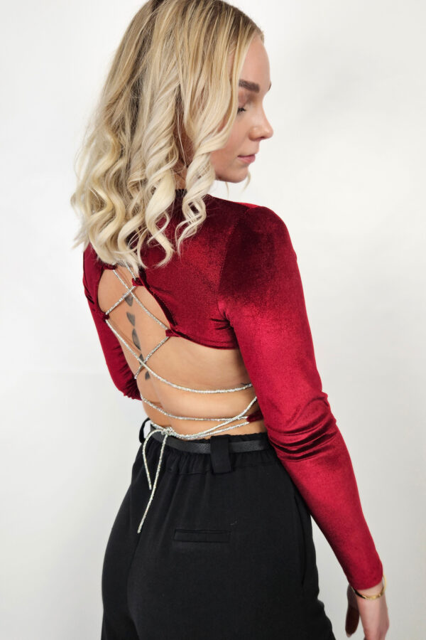 Das rückenfreie Cropped Oberteil aus hochwertigem Samtstoff in dunkelrot ist die perfekte Wahl für besondere Anlässe. Mit langen Ärmeln und einem klassischen Rundhalsausschnitt kombiniert es Eleganz und Komfort. Die auffällige Strassband-Schnürung auf der Rückseite sorgt für einen glamourösen Akzent und lässt das Oberteil besonders chic wirken. Der extrem elastische Stoff passt sich wunderbar der Figur an und betont die Silhouette vorteilhaft. Durch die funkelnden Details ist dieses Party Top ideal für festliche Events und garantiert, dass du im Rampenlicht stehst. Egal, ob du zu einer Feier, einem Abendessen oder einer besonderen Veranstaltung eingeladen bist, dieses Oberteil verleiht deinem Outfit das gewisse Etwas.