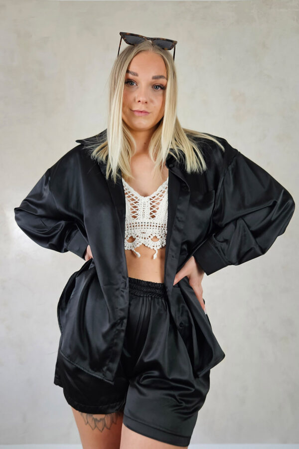 Eine glänzende Satinshorts in schwarz mit einem elastischen Bund für Tragekomfort. Die Shorts haben seitliche Taschen und eine angenähte Reißverschlussblende. Perfekt kombinierbar mit einer passenden Satinsbluse für ein harmonisches und stilvolles Outfit.