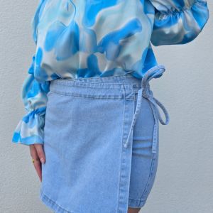 Stilvoller Jeans Skort im Wickel-Look aus hellem Denim-Blau mit seitlicher Schleife zum Binden, integriertem Reißverschluss und Metallknopf. Der Skort verfügt über praktische Hosentaschen hinten und eine kurze Innenhose für maximalen Komfort und volle Bewegungsfreiheit – perfekt für Citytrips, Festivals oder entspannte Tage am Strand.