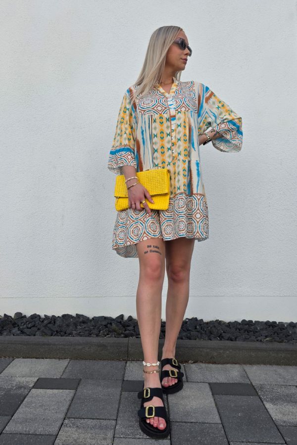 Dieses leichte Boho Kleid mit Knopfleiste ist aus luftigem, fließendem Stoff gefertigt und mit einem auffälligen Ethno-Muster in Blau, Braun und Gelb verziert. Der kurze, lockere Schnitt in knieumspielender Länge sorgt für Bewegungsfreiheit, während der V-Ausschnitt und die 3/4-Ärmel mit leichtem Puff-Effekt dem Kleid eine feminine und sommerliche Note verleihen.