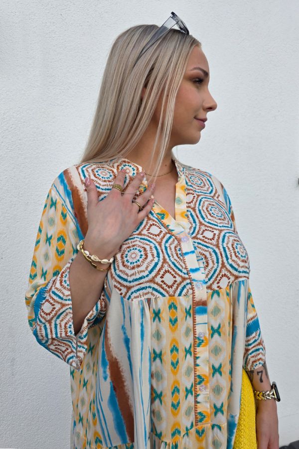 Dieses leichte Boho Kleid mit Knopfleiste ist aus luftigem, fließendem Stoff gefertigt und mit einem auffälligen Ethno-Muster in Blau, Braun und Gelb verziert. Der kurze, lockere Schnitt in knieumspielender Länge sorgt für Bewegungsfreiheit, während der V-Ausschnitt und die 3/4-Ärmel mit leichtem Puff-Effekt dem Kleid eine feminine und sommerliche Note verleihen.